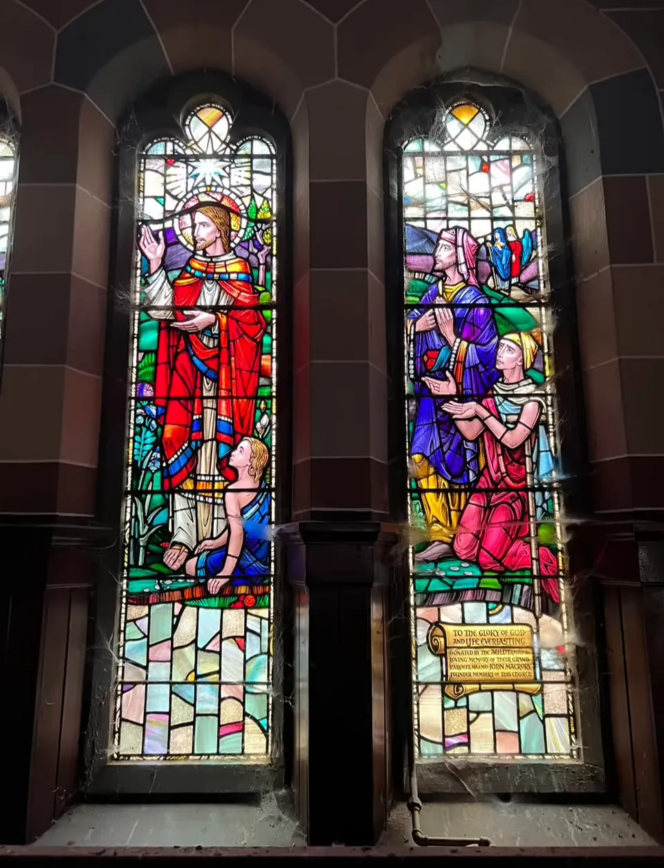 A pair of stained-glass windows with robed figures beneath pointed arches